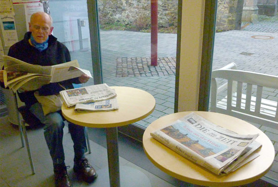 Ein Mann sitzt im Foyer der Bibliothek und liest Zeitung.