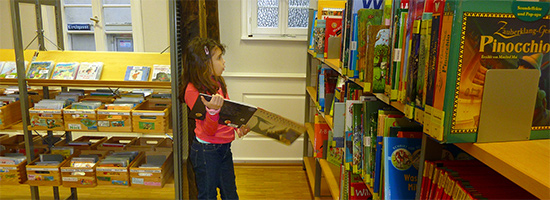 Mädchen mit Buch in der Hand betrachtet Bücherregal