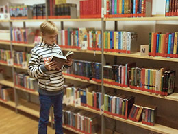 Medienkatalog: Junge stöbert vor vollem Bücherregal.