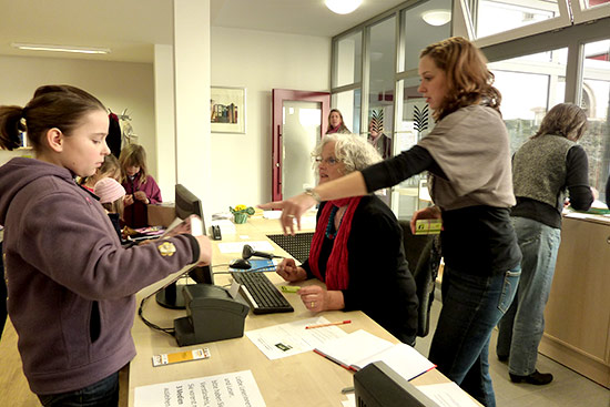 Foto: Eine junge Bibliotheksnutzerin an der Ausleihe. Anne Dietz berät eine Mitarbeiterin.