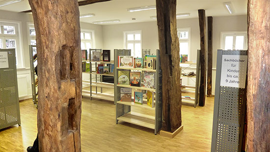 Foto des Innenraums der neuen Bibliothek mit Bücherregalen. Die freien uralten Balken des Gebäudes sind zu sehen.