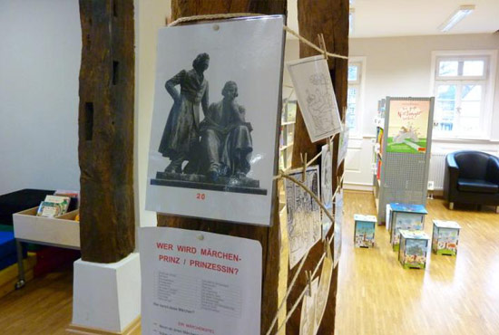 Ausstellung in der Licher Stadtbibliothek. Unter anderem zu sehen: Bilder, die mit Holzklammern an gespannten Schnüren befestigt sind.