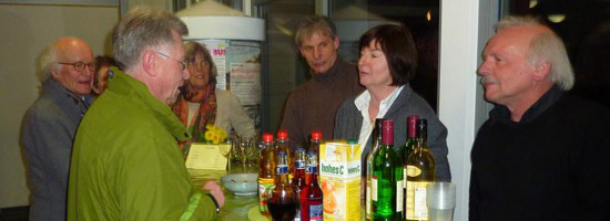 Abendliche Veranstaltung: Eine Gruppe von Personen steht versammelt um einen Tisch mit Getränken.
