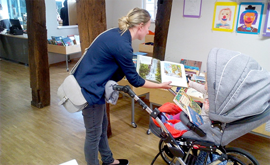 Mutter zeigt Kind in Kinderwagen ein Buch